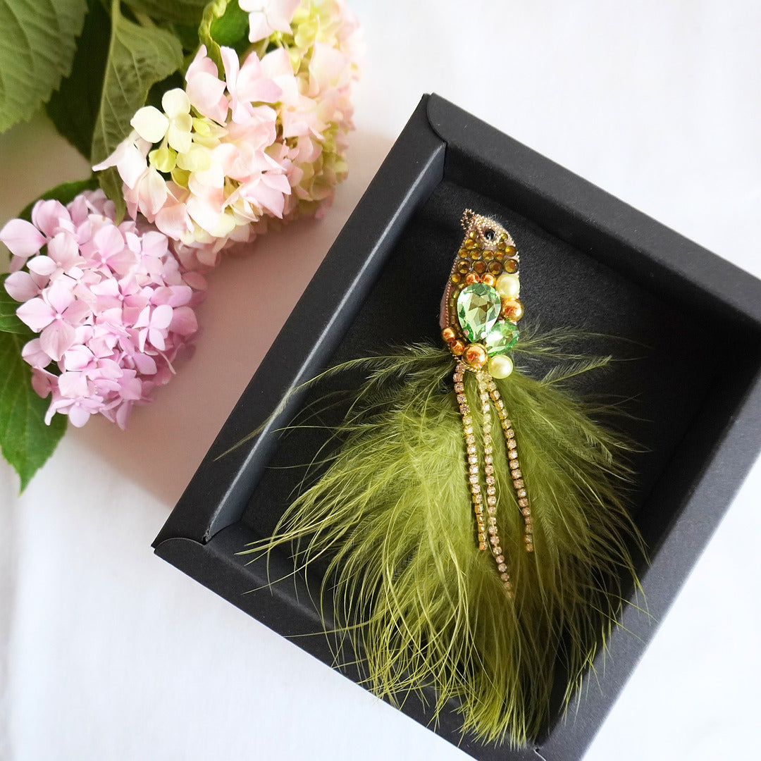 Handmade beaded bird brooch with olive green and gold gemstones, beads and feathers in a box