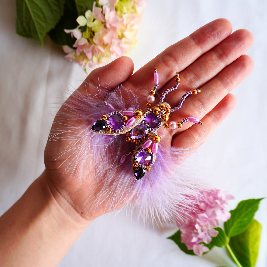 Hand holding a decorative fly TGbrooch with pink feathers and gemstones