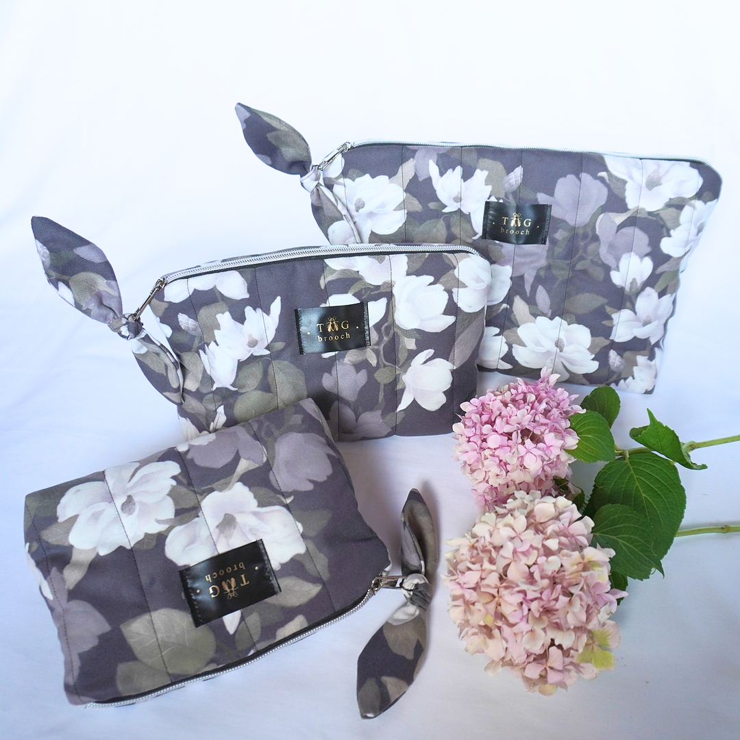 Set of floral-patterned pouches with a brand label on a white background, accompanied by pink flowers - TGbrooch