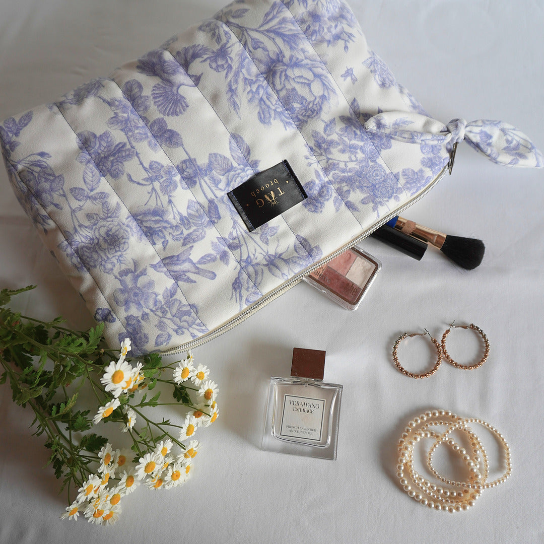 Floral-patterned makeup bag with beauty products and accessories on a white surface - TGbrooch