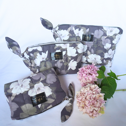 Set of floral-patterned pouches with a brand label on a white background, accompanied by pink flowers - TGbrooch